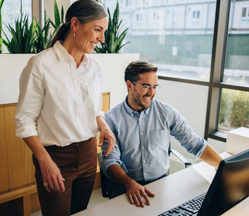 Two coworkers smiling while looking at a computer